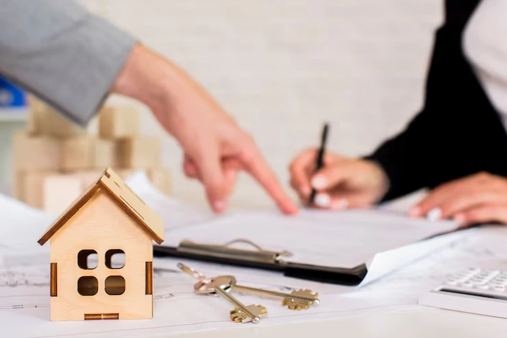 Property consultant explaining investment documents to client with wooden house model and keys on desk