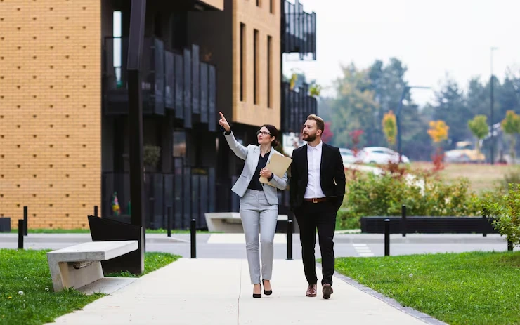 Property consultant pointing out development features to client while walking past modern residential building