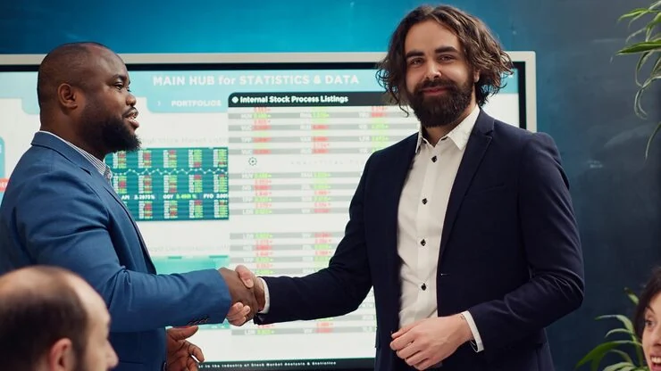 Two property professionals shaking hands in front of investment tracking board showing market data and listings