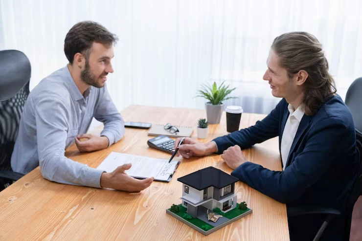 Property advisor discussing acquisition strategy with client using documents and house model in office meeting