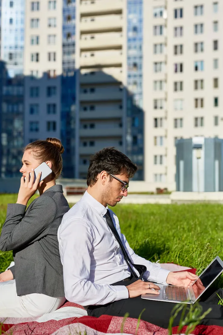 Business professionals working outdoors with laptop and phone near modern apartment buildings
