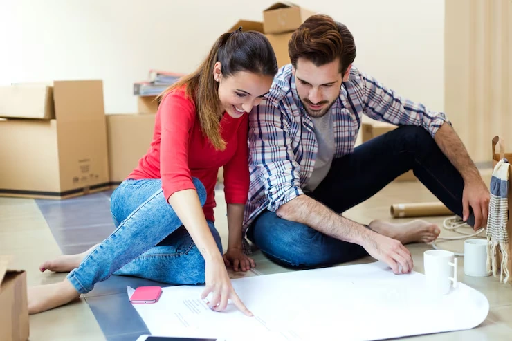 Young couple reviewing renovation plans on floor surrounded by moving boxes in new property
