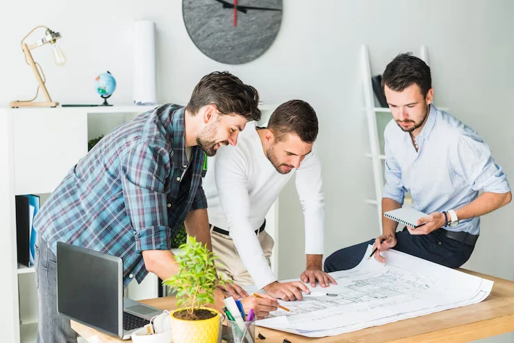 Three project managers reviewing renovation blueprints and plans on desk in modern office