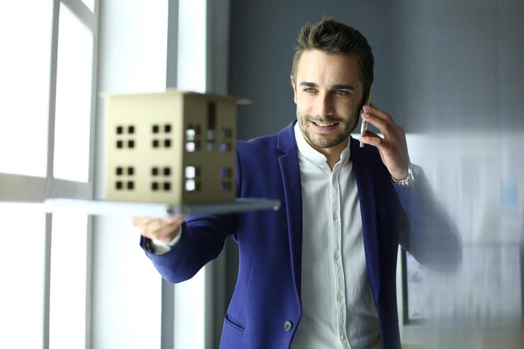 Professional property agent in blue suit making phone call while holding documents in modern office