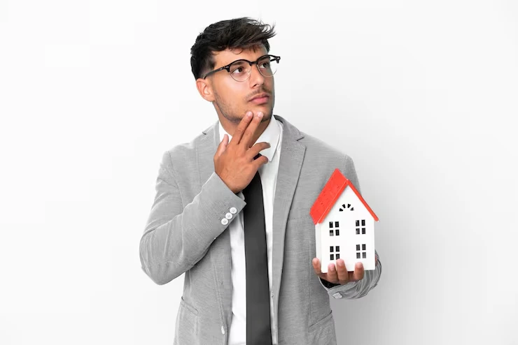 Professional property expert in suit thoughtfully considering house model while evaluating investment options