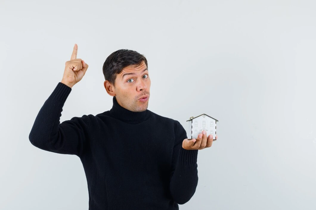 Man pointing upward with excited expression while holding small house model, suggesting property investment success