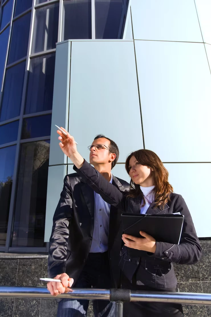 Property sourcing specialists analyzing commercial building exterior with tablet and pointing upward