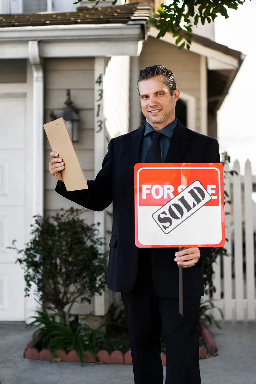 Successful property agent holding sold sign and documents outside residential property after completed transaction