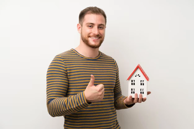 Happy man giving thumbs up while holding house model showing property sourcing satisfaction