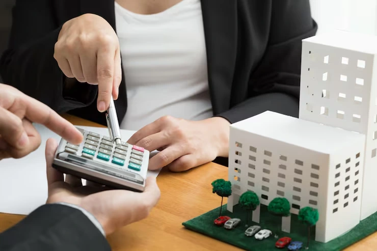 Property finance specialist calculating investment returns using calculator and building models on desk