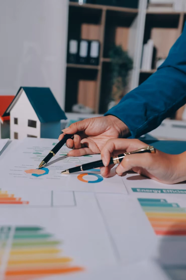 Property analyst reviewing financial charts and data with house model during risk assessment process