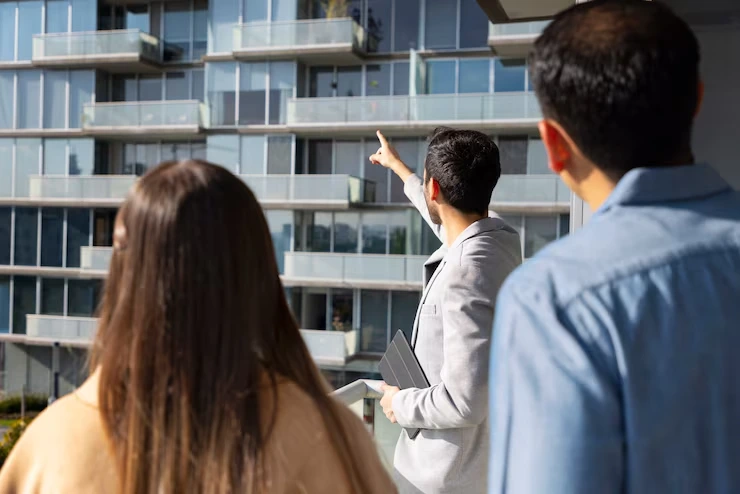 Property agent pointing to apartment building while explaining features to two potential buyers