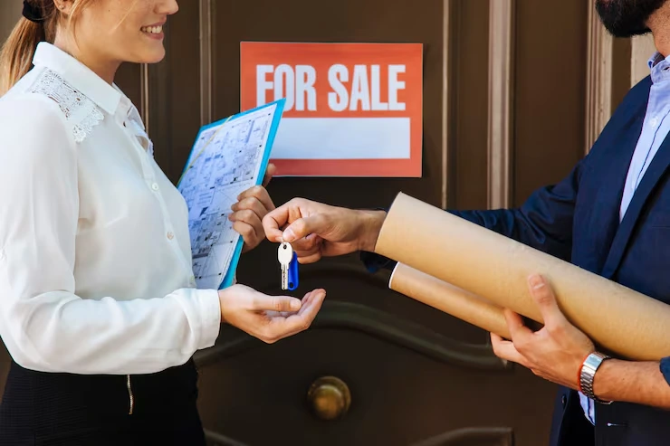 Property agent handing keys to client with documents and for sale sign in background