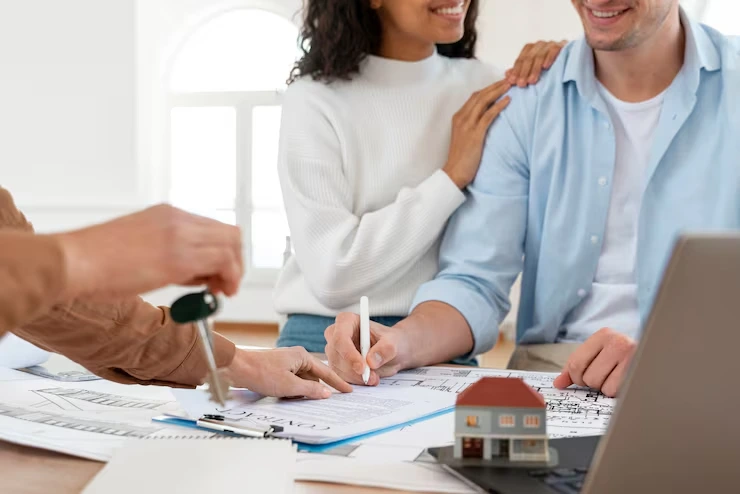 Happy couple signing property purchase documents while advisor hands over house keys with model home on desk