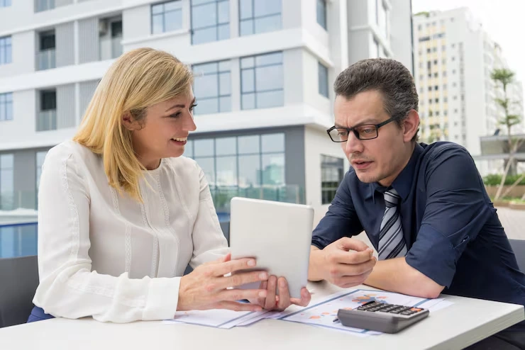 Property advisor using tablet and calculator to explain investment returns to client at outdoor meeting table