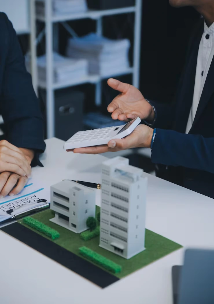 Property consultant explaining investment returns using building model and financial documents with calculator