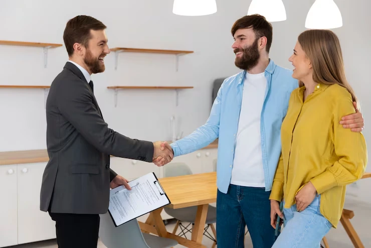 Property agent shaking hands with young couple after successful negotiation in modern office