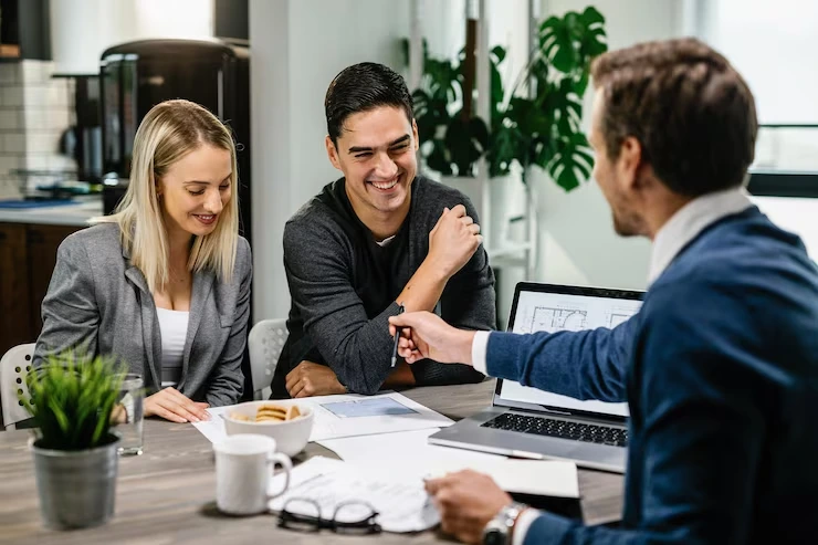 Property advisor shaking hands with smiling couple after successful negotiation with laptop and contracts visible