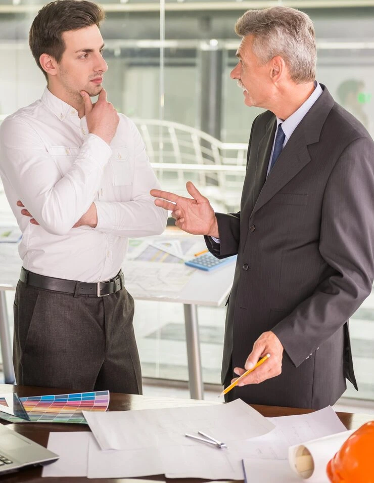 Senior property advisor explaining deal terms to client during negotiation meeting with documents and plans