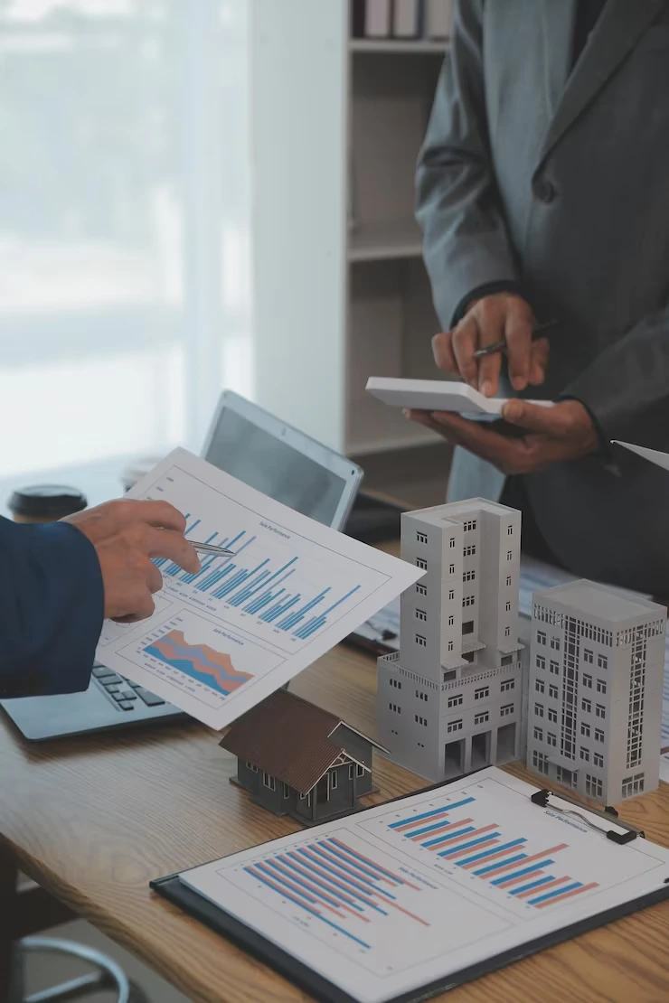Portfolio managers analyzing property performance data with building models and financial charts on tablet