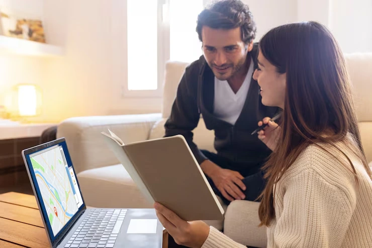Couple reviewing property documents and digital map on laptop during property search consultation