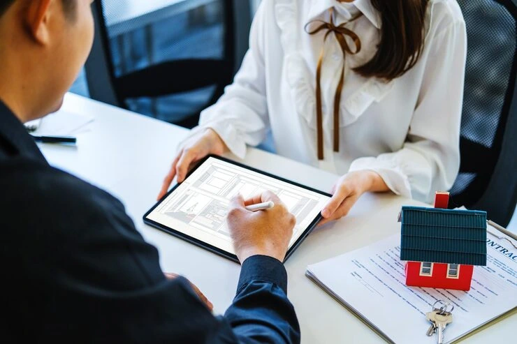 Property consultant reviewing tenant application documents on tablet with client while house model and keys sit on desk