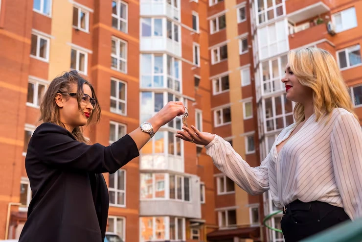 Property agent handing keys to client after completing BRR investment purchase outside apartment building