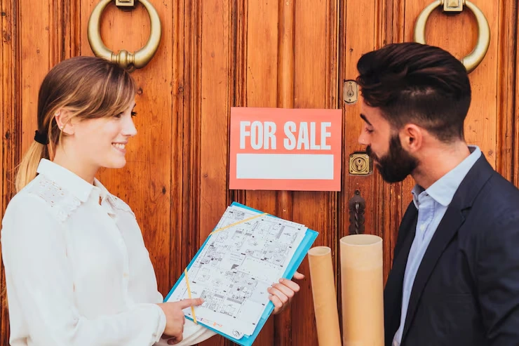 Real estate agent showing property floor plans to investor outside house with for sale sign